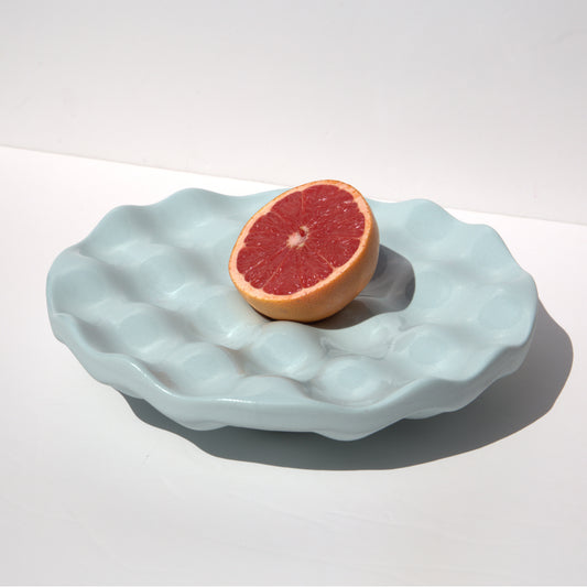 Light blue textured bowl with a halved grapefruit on a white background